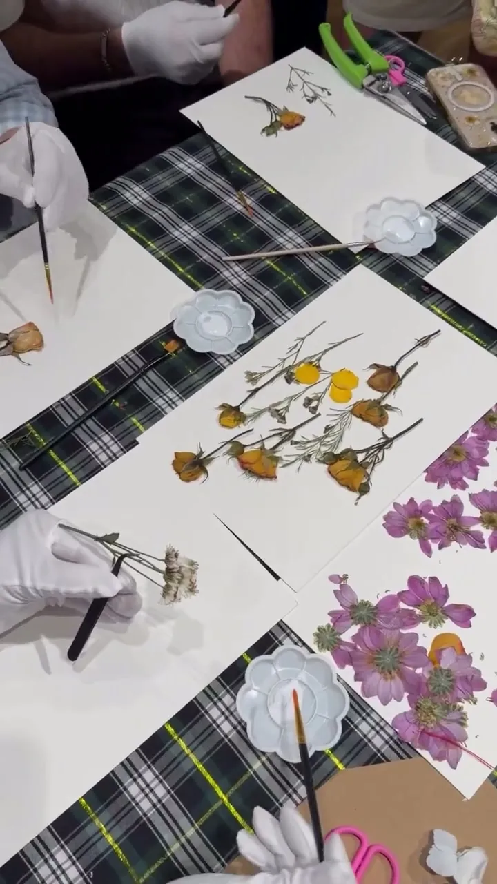 Manos con guantes blancos componen flores prensadas en el taller Herencia botánica para Barbour