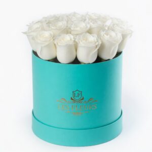 White roses arranged in a turquoise hatbox-style container with a gold Les Fleurs logo, centered on a white background.