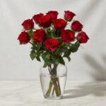 Bouquet of red roses in a clear glass vase with water on a marble table.