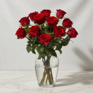 Bouquet of red roses in a clear glass vase with water on a marble table.