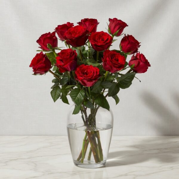 Bouquet of red roses in a clear glass vase with water on a marble table.